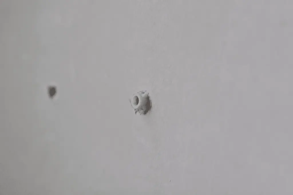 Cheville plastique insérée dans mur blanc avant fixation tasseau