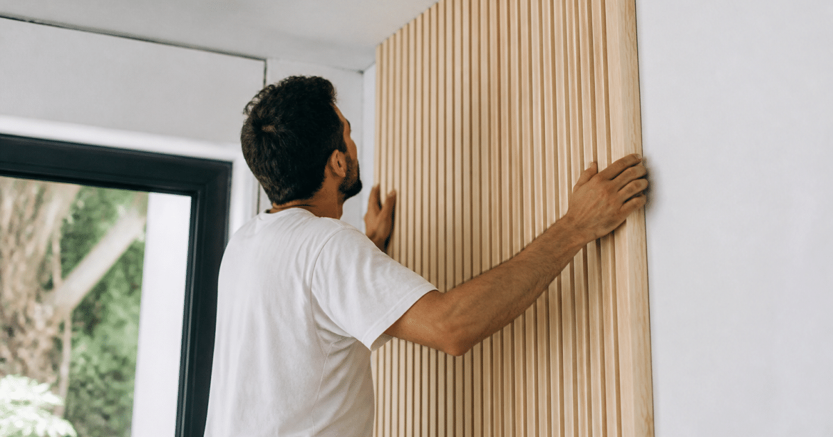 Ouvrier fixant panneaux bois vertical contre mur blanc plâtre