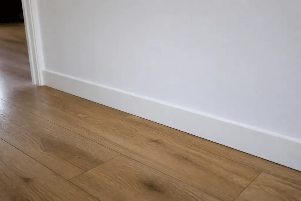 Plinthes blanches fixées au mur au-dessus parquet flottant