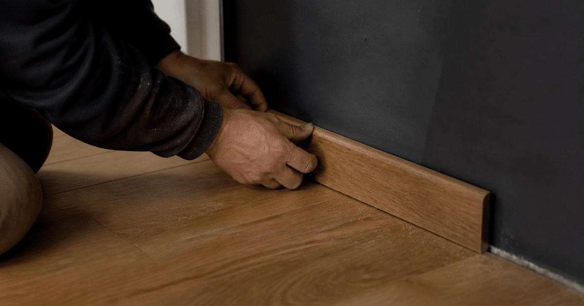 Mains fixant molure finition bois au bas mur parquet