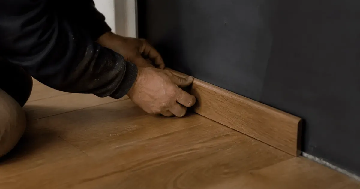 Mains fixant molure finition bois au bas mur parquet