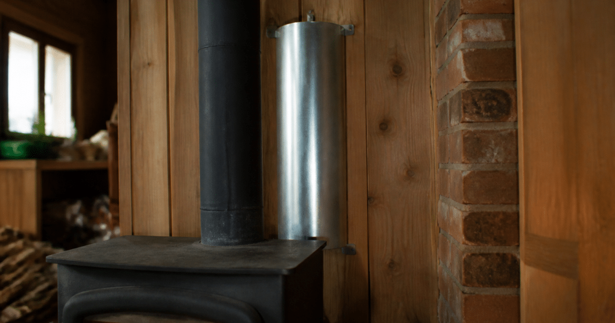 Metal cylinder mounted vertically behind wood stove capturing heat
